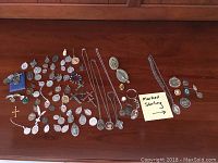Full lot overview of various religious medallions, crosses, and money clips arranged on a wooden surface, showing the assortment and some pieces marked sterling as indicated by a note.