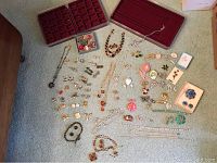 Wide shot showing a collection of vintage costume jewelry items spread on carpet including pins, necklaces, earrings, and jewelry trays lined in red velvet.