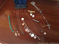 Top-down view of assorted sterling silver and gold-filled jewelry including a turquoise bracelet, charm bracelet, rosary, and various pins and necklaces.