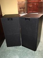 Pair of KEF Q Series Model Q60 speakers with black fabric grilles on, positioned on floor carpet.