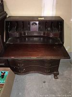 Front view of open drop front desk showing interior pigeonhole compartments, two small drawers inside, decorative columns, and shell-shaped carving in center section.