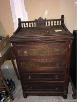 Full front view of the dark wooden Eastlake chest of drawers showing top spindled gallery, multiple drawers with brass ring handles, carved details, and overall condition.