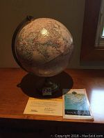 Photo of the full globe on a wooden surface alongside the certificate of authenticity and the 'Your Globe' instructional booklet.