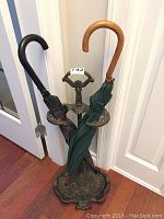 Italian metal umbrella stand holding two umbrellas, showing curved handles and placement of umbrellas