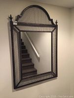 Full view of the wall mirror showing steel frame with mesh grid and arched top with finials.