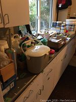 Wide view of countertop showing assorted tools, cleaning supplies, paint cans, and hardware boxes spread out.