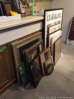Various artwork pieces leaning against counter including framed photographs and paintings with various frame styles and sizes.