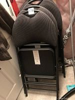 Four stacked black folding chairs with padded seats and backs, showing the seat bottom labels and overall condition