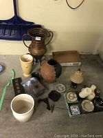 Overall view of the collection of planter pots, candles, lamp, and small decorative items placed on concrete floor.