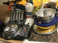 Photo showing toaster, bundt cake pan, waffle iron, trays, and dishes, arranged on countertop.