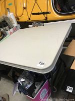 White six-foot folding table from an angled top view showing corner and handle area, plastic surface with minor marks.