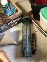 Photo showing bird seed feeder, hummingbird feeder, plastic funnel, box with bird seed packets, and red/black gardening pot.