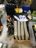 Photo showing the assembled camping lot items in a small storage area including sleeping bag, water bottles, axe, gloves, boots, soft cooler, stool, cushions and other camping accessories.