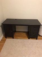 Front view of black-brown Ikea Hemnes desk showing cabinet door on left and two drawers on right with flat top surface