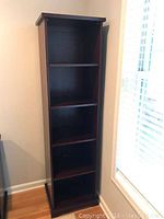 Front view of the narrow, tall mahogany bookcase with five shelves, placed beside a window showing scale and condition