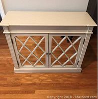 Front view of white console table with mirrored lattice doors on hardwood floor