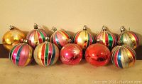 12 colorful striped and solid color vintage Christmas ball ornaments on beige surface.