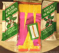 Two unopened packs of green and white icicle garlands and one pack of shiny gold tinsel strands still in packaging.