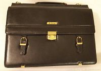 Front view of black imitation leather briefcase with lock and buckles on a white background