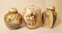 Three hand-painted decorative vases arranged side by side, showing detailed butterfly and floral artwork on cream ceramic bodies with lids.