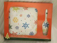 Square ceramic cake plate and matching cake server with multicolored snowflake design, holiday-themed.