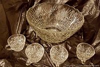 Large clear glass punch bowl and four matching cups with starburst cut pattern on a dark fabric background.