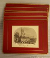 Six red place mats stacked showing central black and white sketch of The College, Gloucester with gold trim around edges.