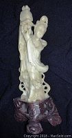 Full view of the carved jade goddess figurine on a wooden stand showing detailed carving and smooth jade finish.