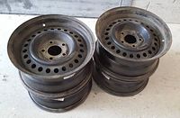 Photo of four black steel rims stacked showing bolt pattern and ventilation holes, used condition.
