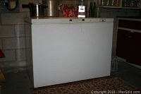 Front view of the W.C Woods deep freezer showing the whole unit with no contents, placed in a basement or storage area.