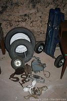 Overview photo showing four tires in front, a blue metal cart frame with wheels on the right, claw foot tub legs and various small mechanical parts laid out on the floor.