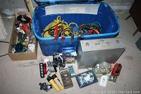 Photo showing blue plastic bin containing yellow rope, tether straps, an aluminum tool/carrying case, various flashlights, batteries, headlamp, and other electrical accessories placed on floor.