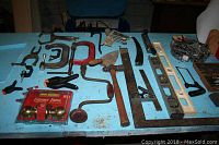 Overview of various clamps, hand saws, spirit levels, hammer, metal hand tools, and a packaged door knob set on a blue table.