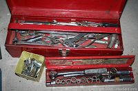 Red metal tool box opened showing wrenches, ratchets, and other hand tools.