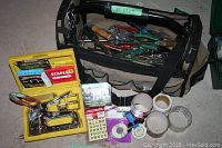 Photo showing the canvas tool bag filled with various hand tools including screwdrivers and pliers, along with the yellow plastic case containing the Arrow staple gun and staples.