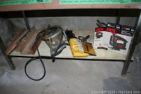 Photo showing three main power saws and several wooden miter boxes on a metal shelf in a concrete area.