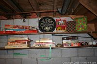 Two-tier shelf with vintage boxed board games including Aurora Skittle Score Ball and Rebound, dartboard, lawn darts and game boards