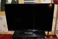 Front view of Samsung 46\" LED TV on stand with remote placed on shelf.