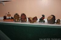 Full view of six items on white shelf: oak leaf face bookend, mechanical trick dog toy, bird figurine, wooden log piece, brass face sculpture.