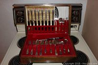 Photo showing the 1881 Rogers Triple silverware set arranged in a wooden case with red velvet lining, including the Certificate of Authenticity and various utensils in place