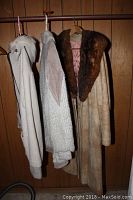 Photo showing three coats hanging on wooden wall, including the leather suede coat with fur collar and the lighter colored sweater coat.
