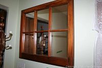 Pine framed mirror with divided glass panes hung on wall, with coat rack reflected.