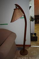 Full view of the wooden floor lamp next to a sofa, showing its height and curved design.