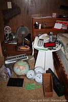 Overview of lot showing side tables, telephones, alarm clocks, globe, clocks, bags with miscellaneous items