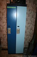 Front view of two metal school lockers side by side, one blue door and one light blue door with recessed handles and lock slots.