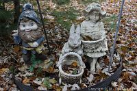 Garden gnome, rabbit figurine, and girl figurine with baskets among outdoor leaves.