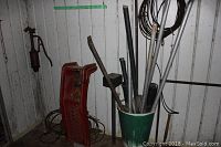 Photo showing two red metal car ramps, a green and white container holding various metal rods, a wall-mounted metal oil pump, and a manual winch on floor.