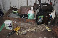 Close-up of the wooden crate and contents including screws, nails, green bottle of oil, wire cutters, rope with hooks, and an oil canister beside black plastic oil containers.