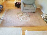Full view of the pink rectangular area rug with a central paisley floral design, placed on hardwood floor beneath armchairs and adjacent to other furniture.