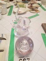 Three clear glass items on a table with green tape around: a glass elephant figurine, a glass snail figurine, and a clear glass swirl paperweight.